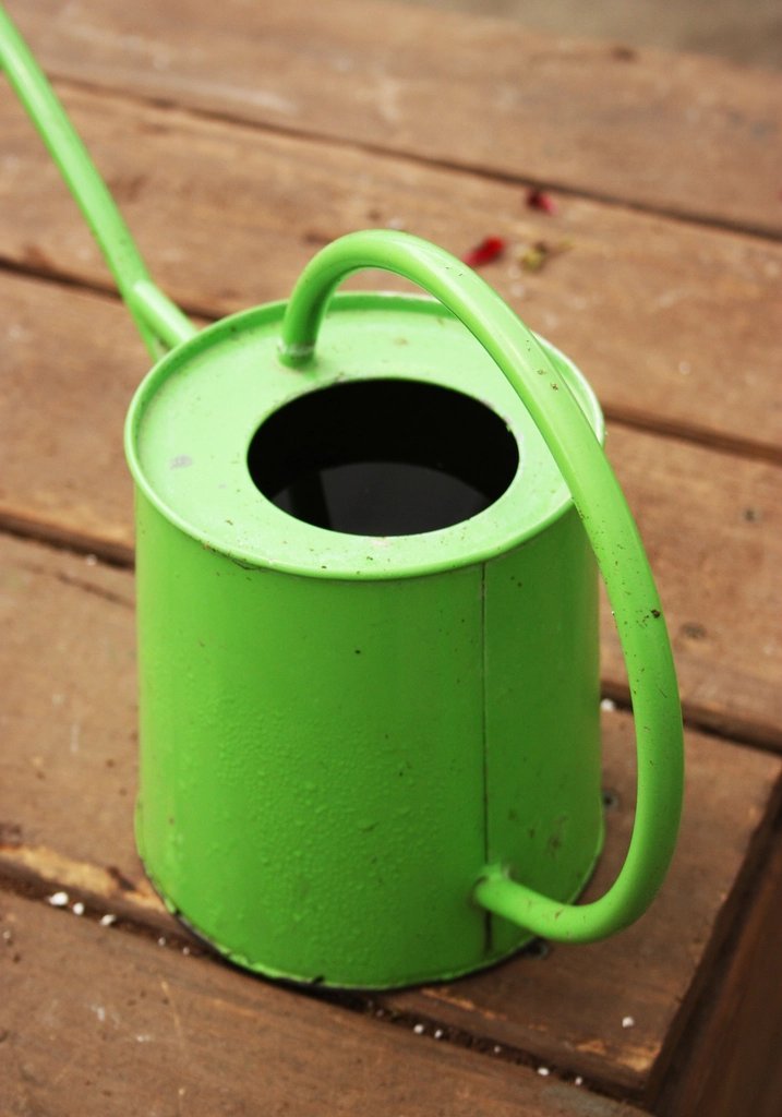 Green metal watering can on a wooden garden table