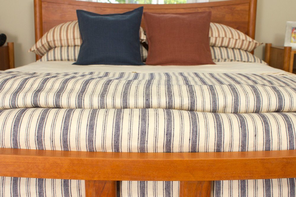 Blue and ecru striped cotton throw on a bed with two cushions