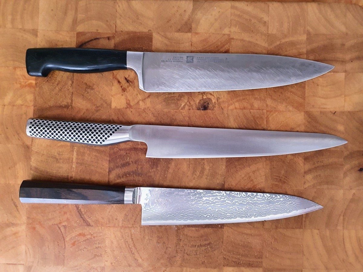 Thick wooden chopping board with three kitchen knives on top