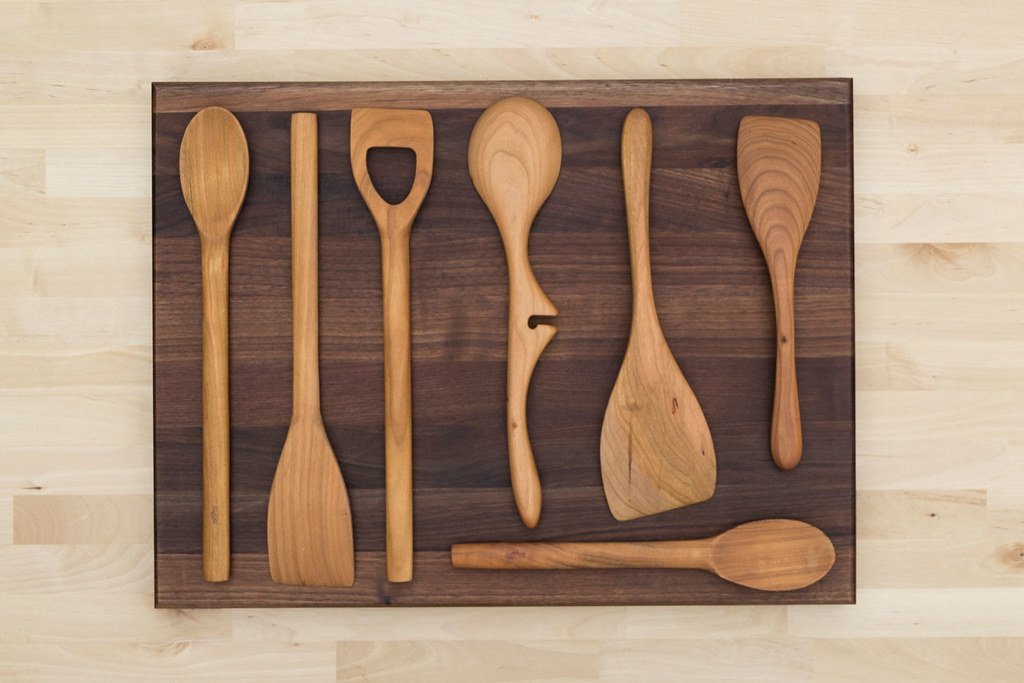 Seven wooden kitchen utensils lined up on a board